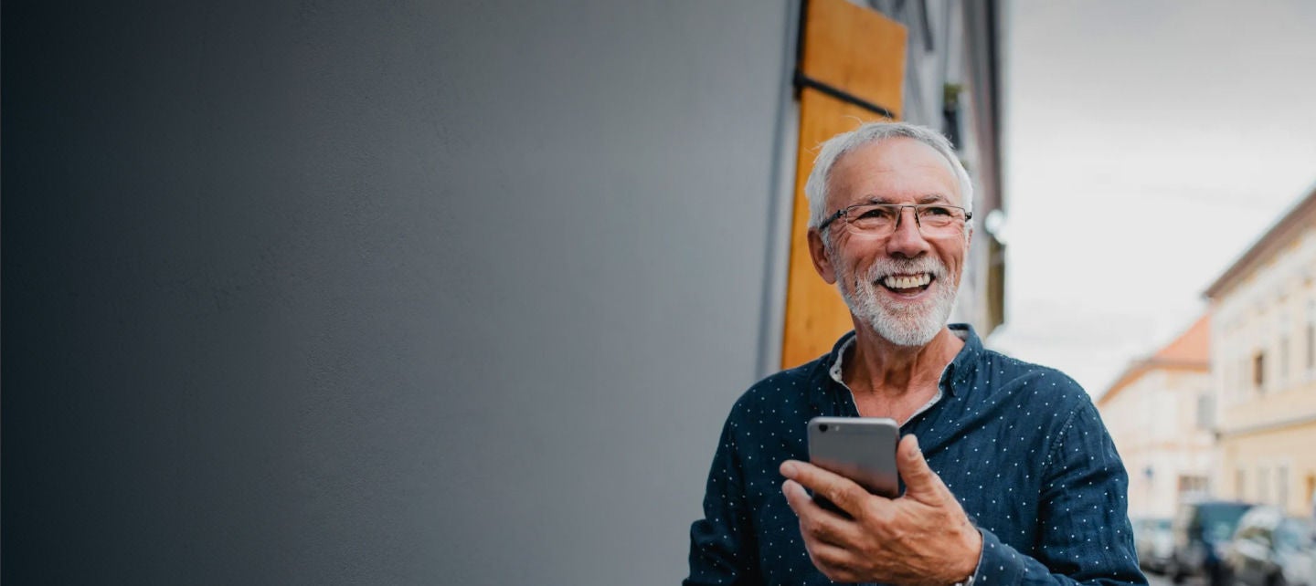 smiling senior man using phone on street