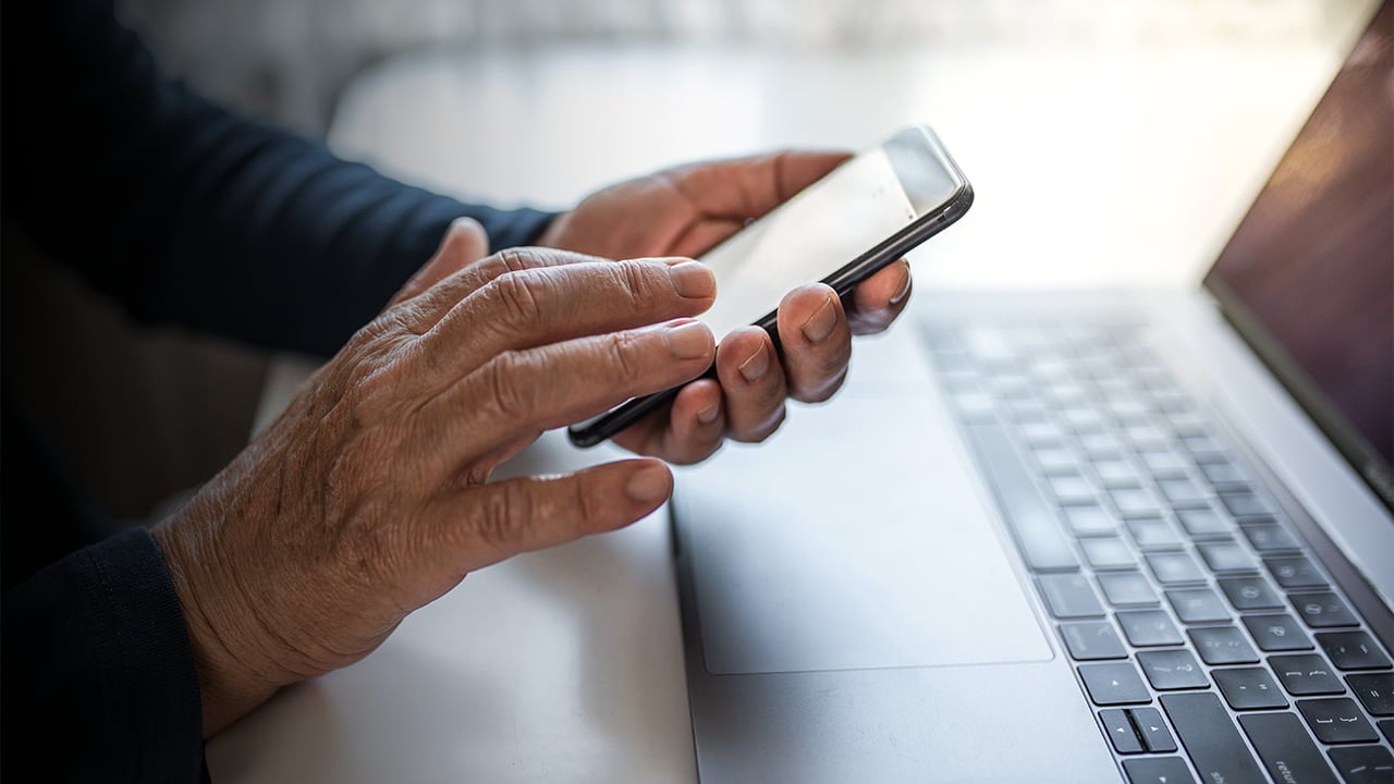 hands using smartphone near laptop