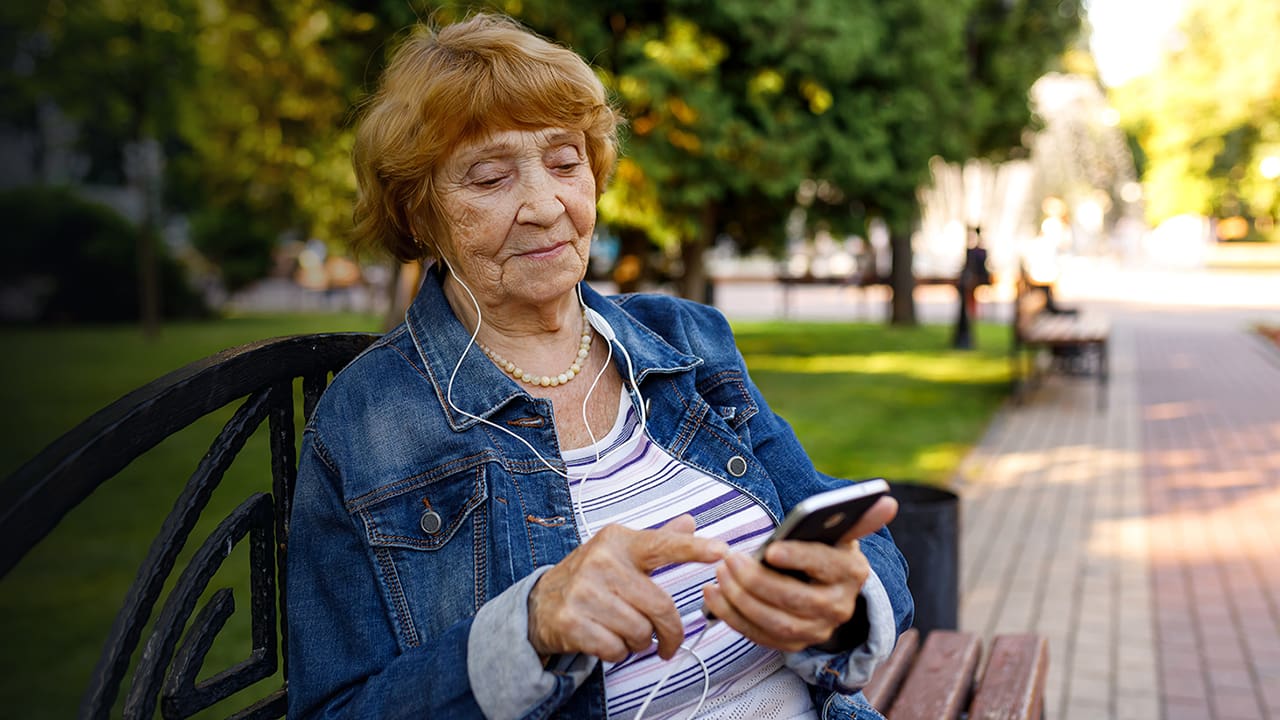 senior woman with headphones using phone outdoors