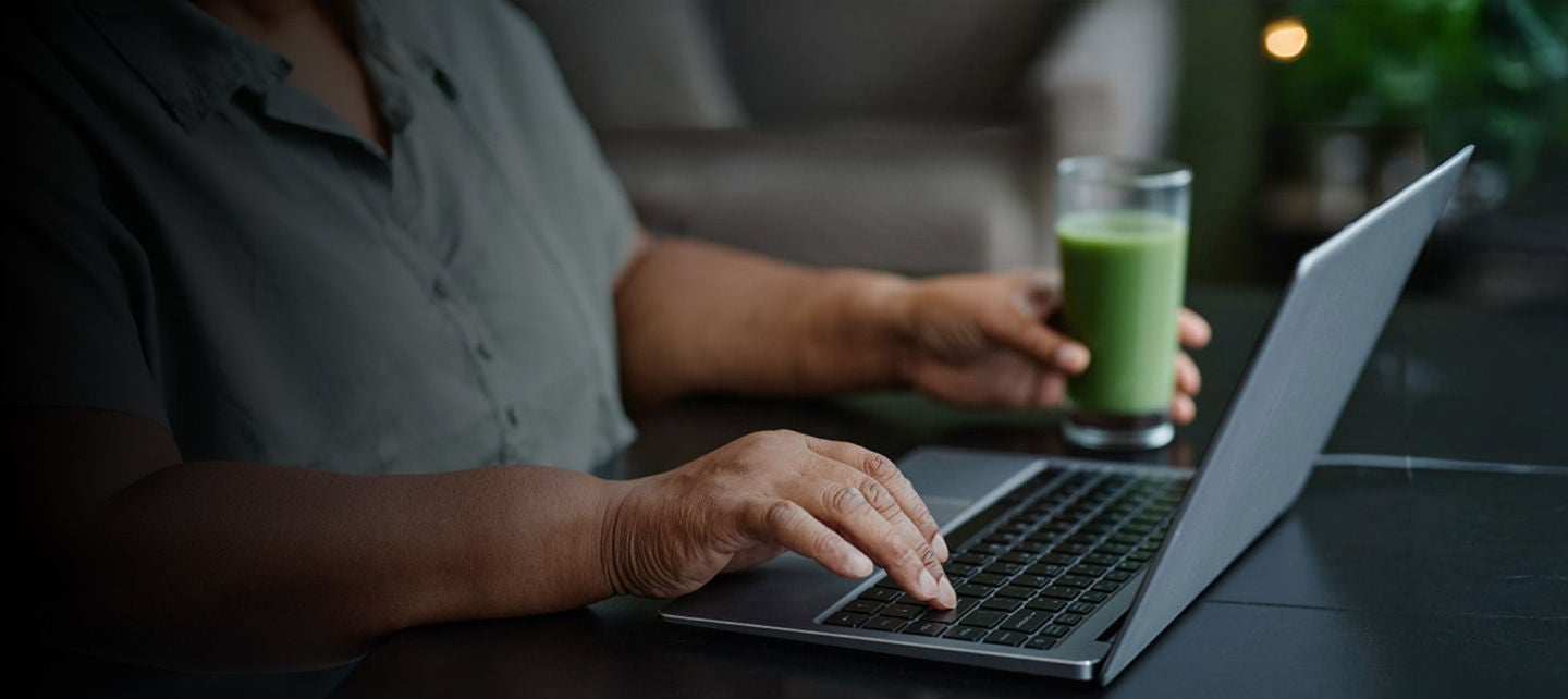woman using laptop drinking smoothie