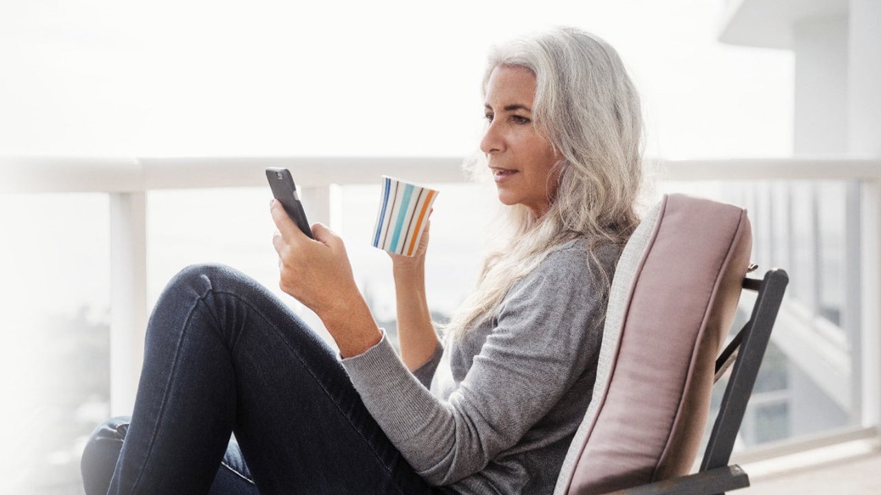 woman relaxing with phone and coffee on balcony