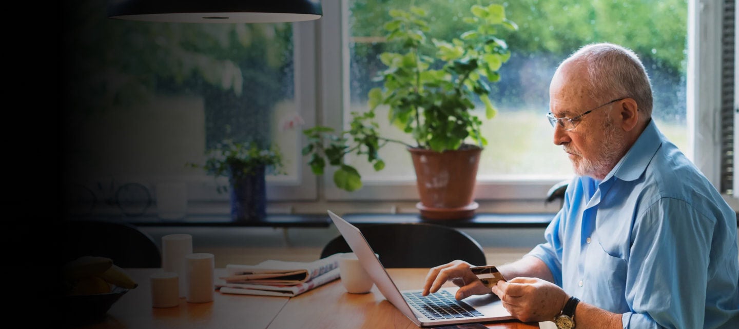 senior man paying bills with laptop and card