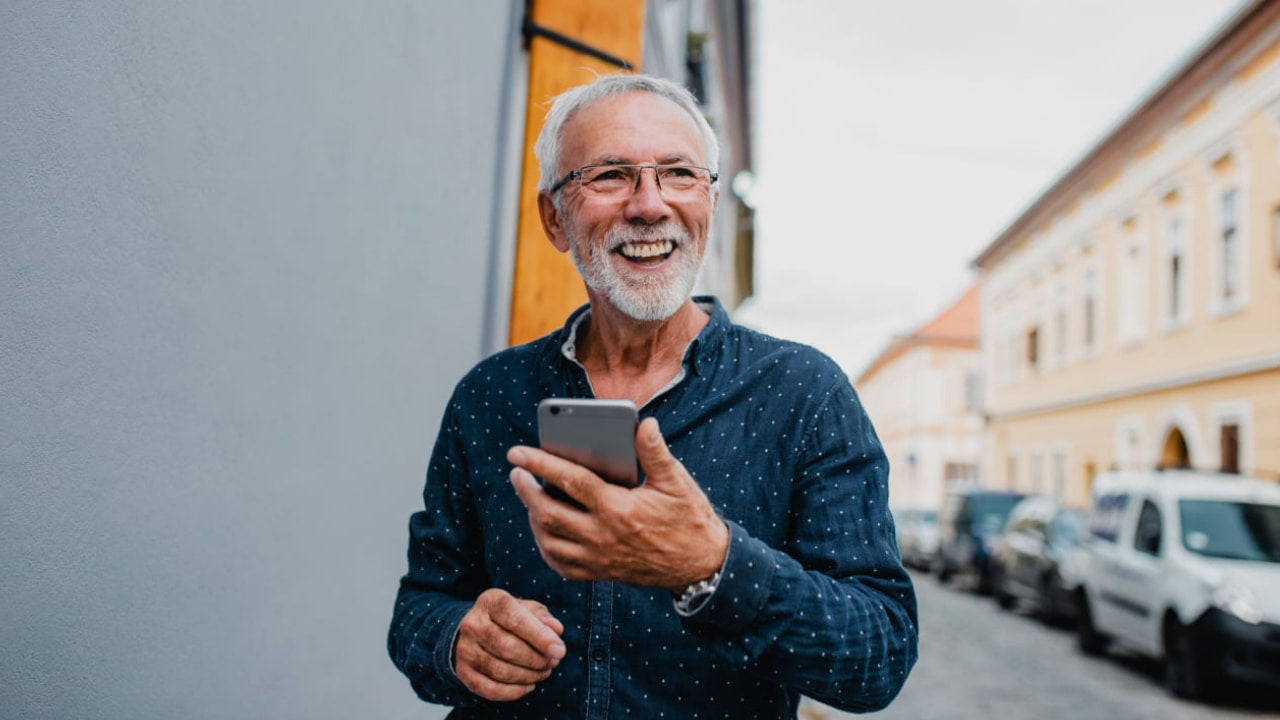 smiling senior man using phone on street