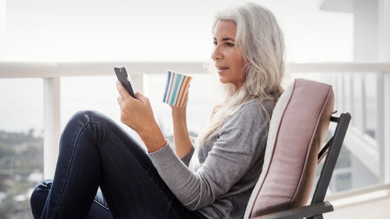 woman relaxing with phone and coffee on balcony