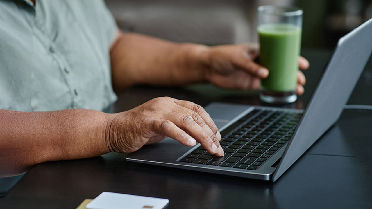 woman using laptop drinking smoothie