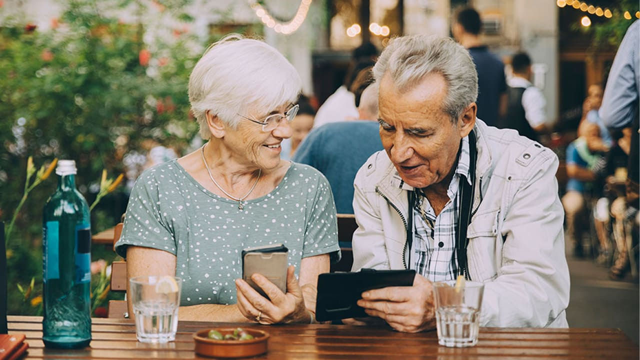 senior couple using devices at cafe