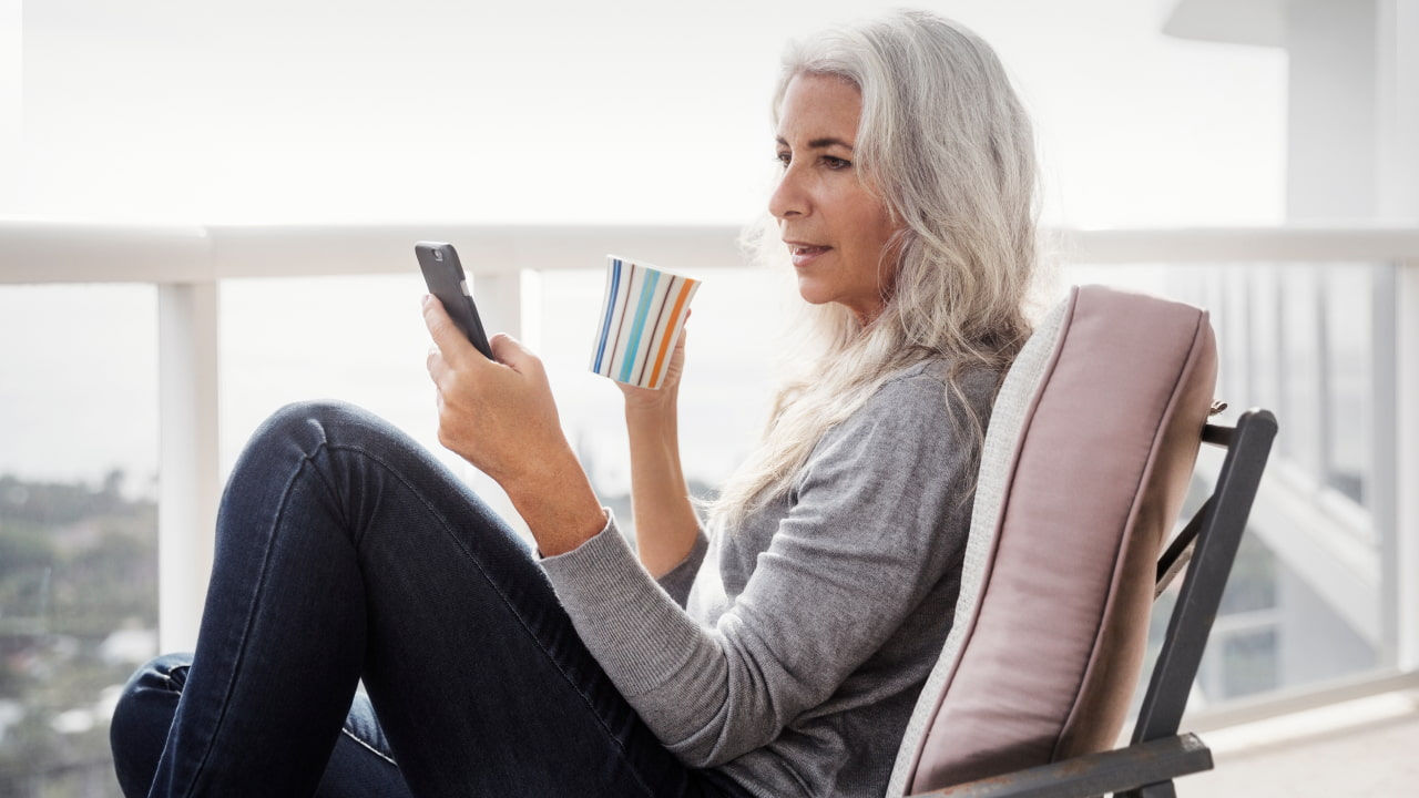woman relaxing with phone and coffee on balcony