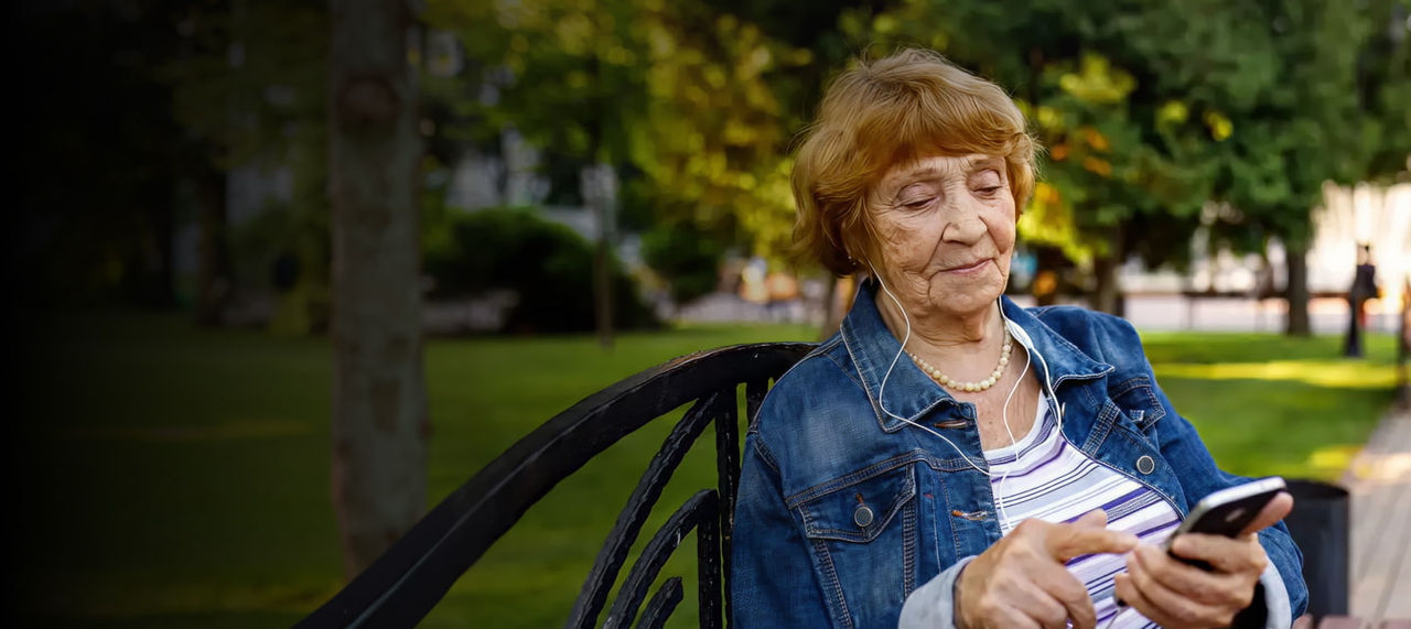 senior woman with headphones using phone outdoors