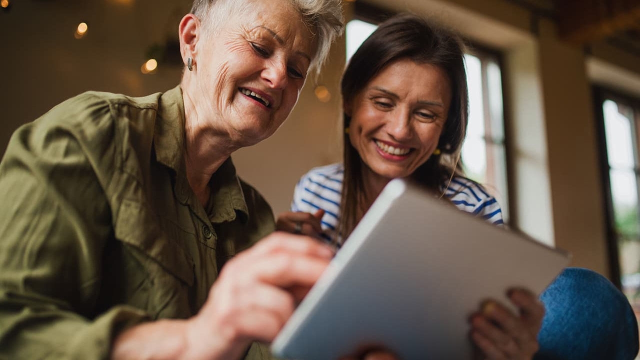 woman helps older woman on tablet
